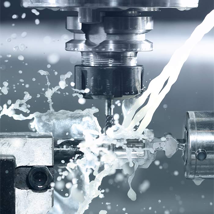 A close-up shot of a CNC milling machine in operation, with a cutting tool actively machining a metal workpiece while coolant sprays and splashes across the surface